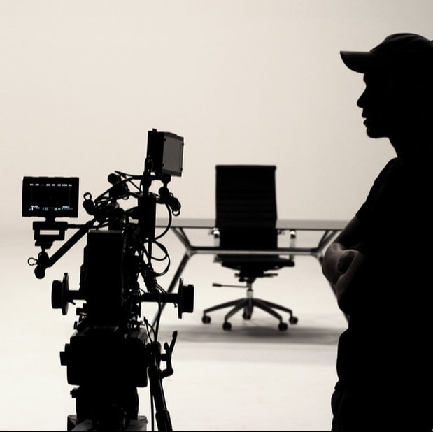 silhouette of male standing next to video camera with desk and chair in background
